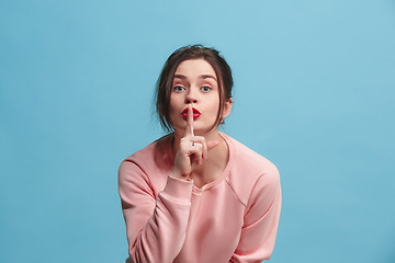 Image showing The young woman whispering a secret behind her hand over blue background