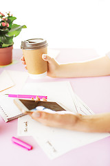 Image showing The female hands holding phone and coffee on trendy pink desk.