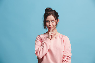 Image showing The young woman whispering a secret behind her hand over blue background