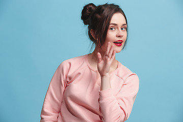 Image showing The young woman whispering a secret behind her hand over blue background