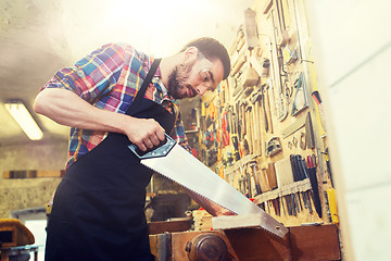 Image showing carpenter working with saw and wood at workshop