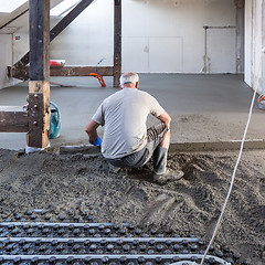 Image showing Laborer leveling sand and cement screed over floor heating.