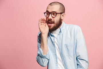 Image showing The young man whispering a secret behind her hand over pink background