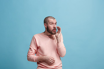 Image showing The young man whispering a secret behind her hand over blue background