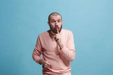 Image showing The young man whispering a secret behind her hand over blue background