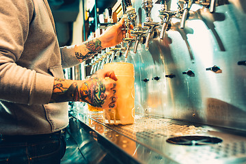 Image showing Hand of bartender pouring a large lager beer in tap.