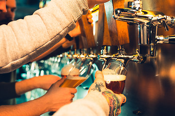 Image showing Hand of bartender pouring a large lager beer in tap.