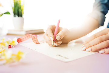 Image showing The female hands holding pen. The trendy pink desk.