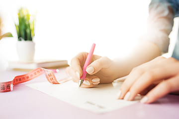 Image showing The female hands holding pen. The trendy pink desk.