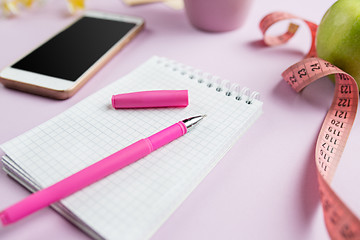 Image showing side view of green apple, measuring tape, mobile phone, pen and open notebook. Fitness Concept.