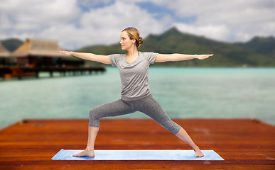 Image showing woman making yoga warrior pose on mat outdoors