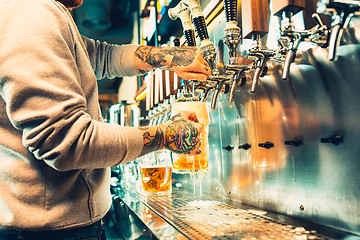 Image showing Hand of bartender pouring a large lager beer in tap.