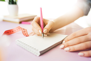 Image showing The female hands holding pen. The trendy pink desk.