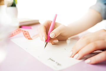 Image showing The female hands holding pen. The trendy pink desk.