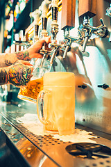 Image showing Hand of bartender pouring a large lager beer in tap.