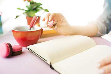 Image showing The female hands holding french macarons on trendy pink desk.