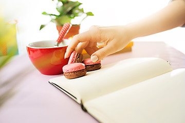 Image showing The female hands holding french macarons on trendy pink desk.