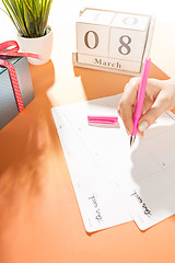 Image showing The side view of orange desk with cup of coffee, gift, flowers and notebook