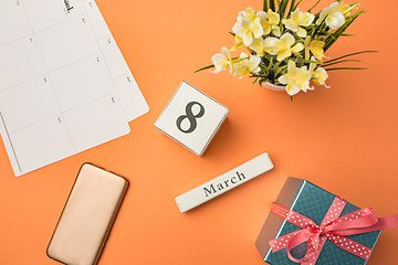 Image showing The top view of orange desk with phone, gift, flowers and notebook