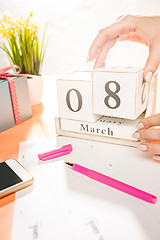 Image showing The side view of orange desk with cup of phone, gift, flowers and notebook