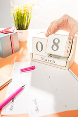 Image showing The side view of orange desk with cup of phone, gift, flowers and notebook