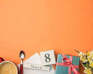 Image showing The top view of orange desk with cup of coffee, gift, flowers and notebook