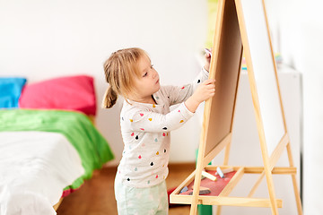 Image showing happy little girl drawing on chalk board at home