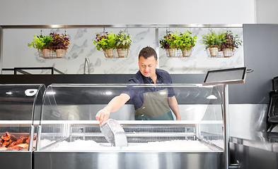 Image showing male seller adding ice to fridge at fish shop