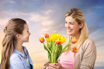 Image showing happy daughter giving flowers to mother over sky