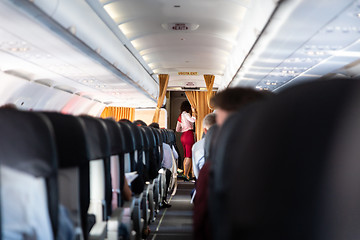 Image showing Stewardess in red uniform on commercial passengers airplane.