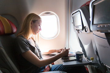 Image showing Casual woman flying on commercial passengers airplane, filling in immigration form.