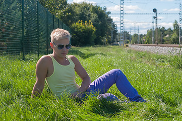 Image showing Young man in yellow t-shirt sitting on the green grass