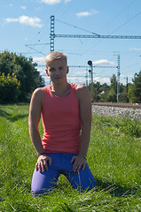 Image showing Young man in orange sitting on the green grass