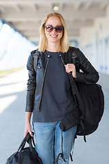 Image showing Portrait of young cheerful female traveler wearing casual clothes carrying heavy backpack and luggage at airport.