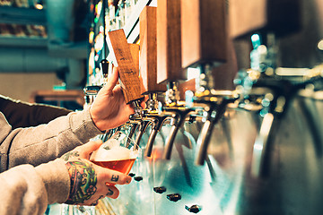 Image showing Hand of bartender pouring a large lager beer in tap.