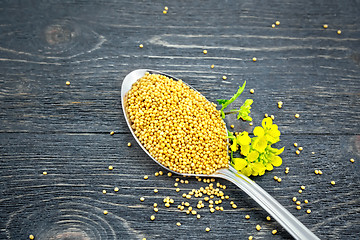 Image showing Mustard seeds in metal spoon with flower on black board