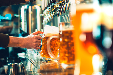 Image showing Hand of bartender pouring a large lager beer in tap.