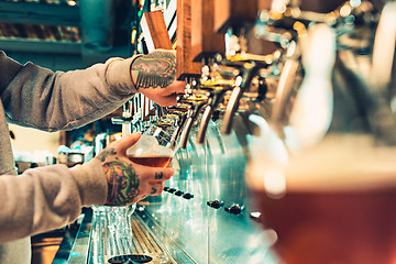 Image showing Hand of bartender pouring a large lager beer in tap.