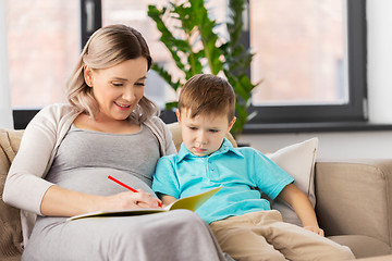 Image showing pregnant mother with workbook and son at home