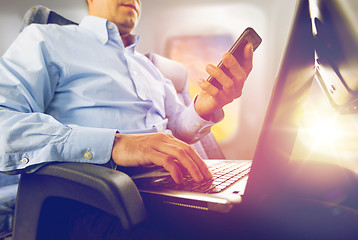 Image showing businessman with smartphone and laptop in plane