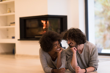 Image showing multiethnic couple lying on the floor  in front of fireplace