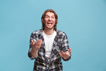 Image showing Beautiful male half-length portrait isolated on blue studio backgroud. The young emotional surprised man