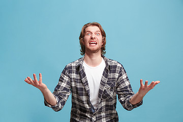 Image showing The young emotional angry man screaming on blue studio background