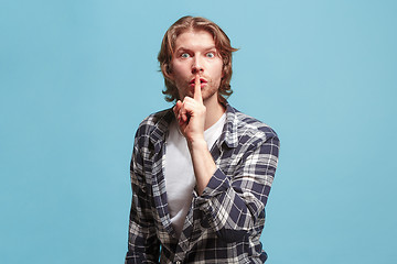 Image showing The young man whispering a secret behind her hand over blue background