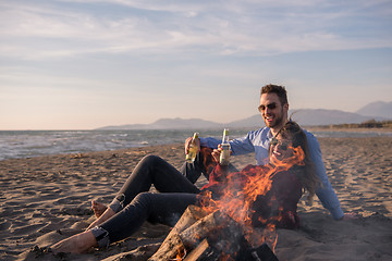 Image showing Young Couple Sitting On The Beach beside Campfire drinking beer