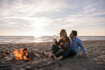 Image showing Young Couple Sitting On The Beach beside Campfire drinking beer