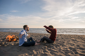 Image showing Young Couple Sitting On The Beach beside Campfire drinking beer