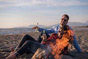 Image showing Young Couple Sitting On The Beach beside Campfire drinking beer