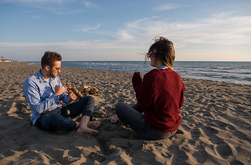 Image showing Young Couple Sitting On The Beach beside Campfire drinking beer