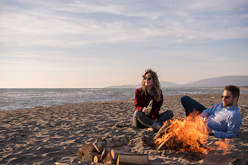 Image showing Young Couple Sitting On The Beach beside Campfire drinking beer